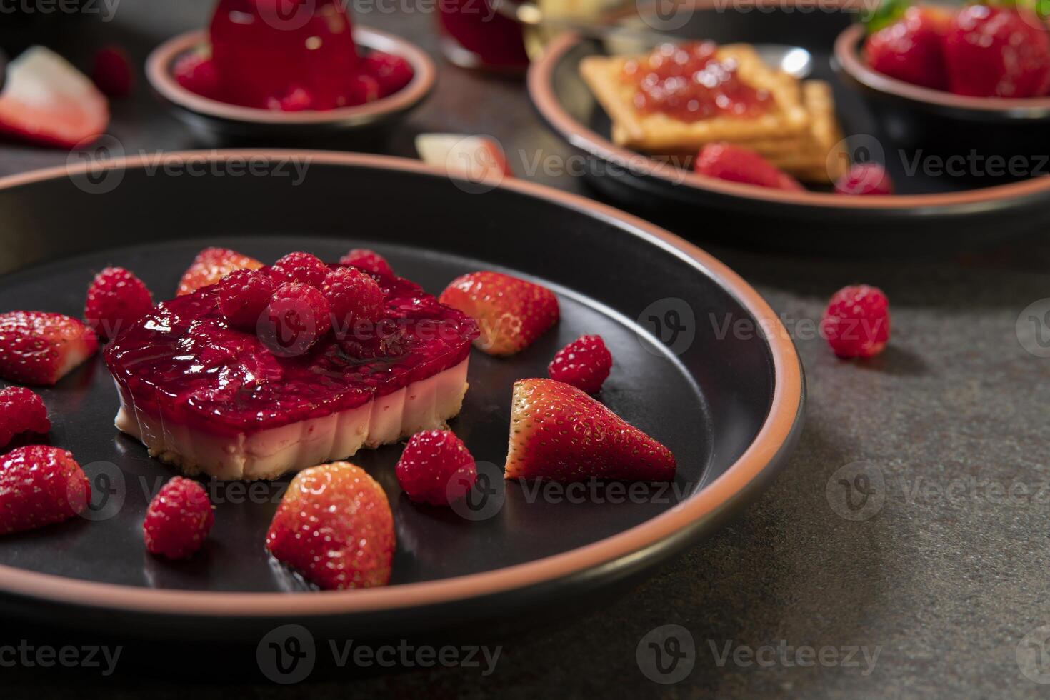 strawberry dessert with raspberries on a black ceramic plate in the foreground against a background of cookies with strawberry jam and strawberry jelly on a black table photo