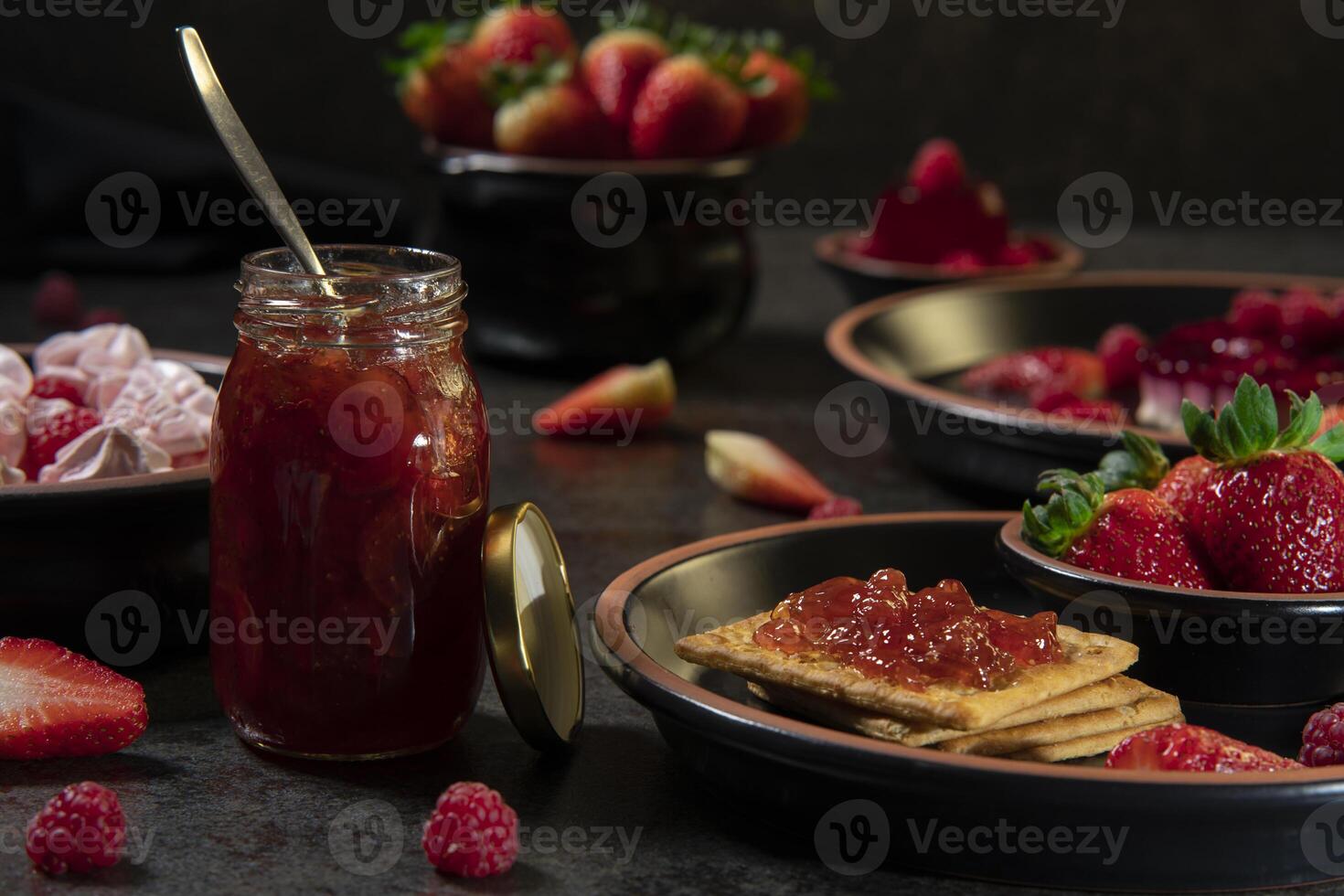 jar of jam next to a plate with cookies and strawberry jam in the foreground against a background of plates with strawberry desserts photo