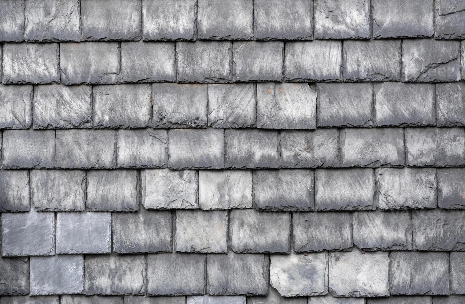 Gray slate roof tiles interlocking tightly, presenting weathered texture and architectural resilience, highlighting traditional roofing craftsmanship with protective surface pattern photo