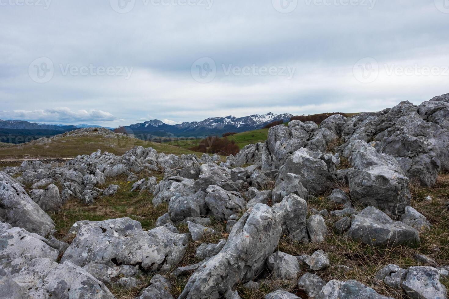Rocky landscape with distant snow capped mountains under a cloudy sky photo