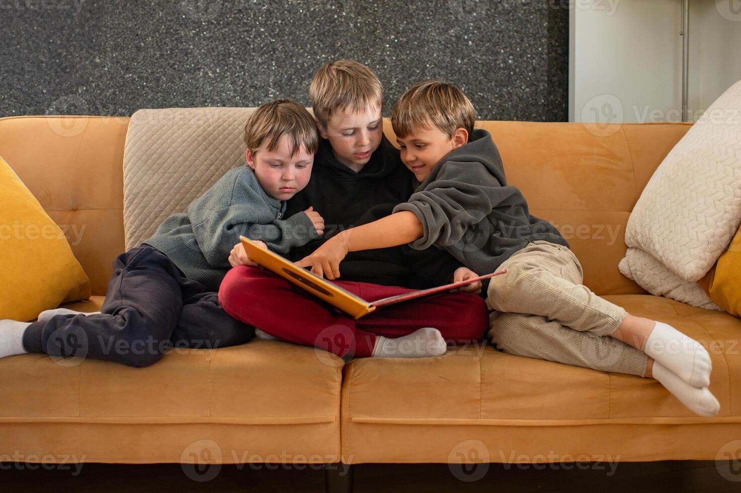 An older brother shares a story with his little siblings on the couch, as they listen with wide-eyed wonder. photo