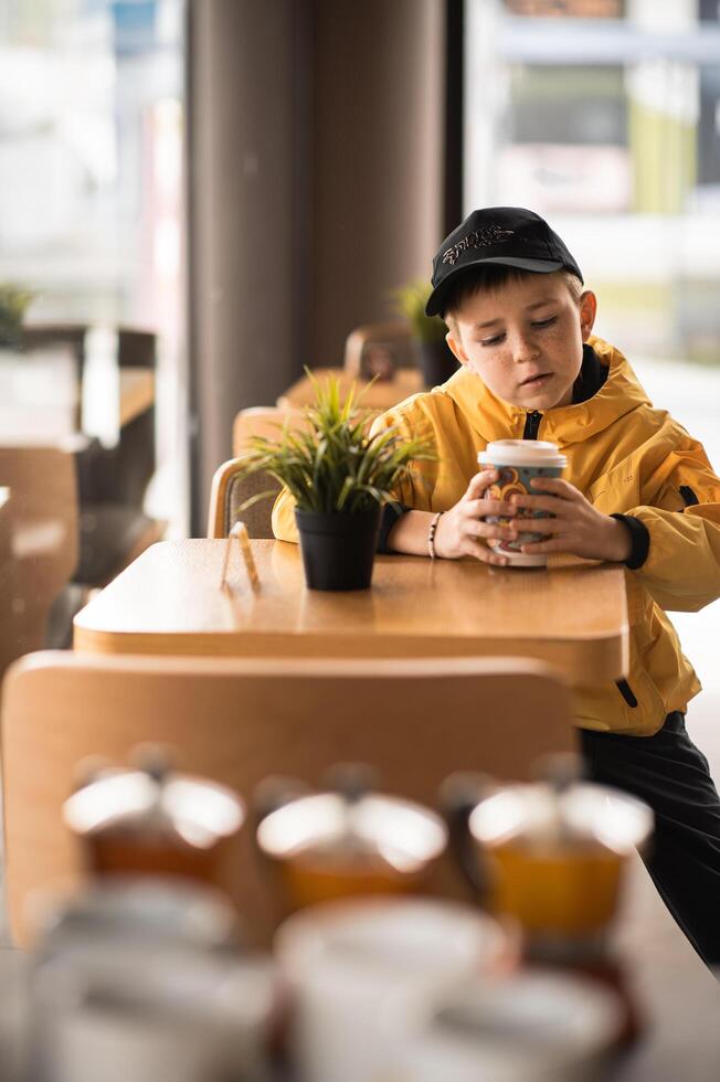 A thoughtful gaze boy in a cap stirs his coffee absentmindedly, as if waiting for something unseen. photo
