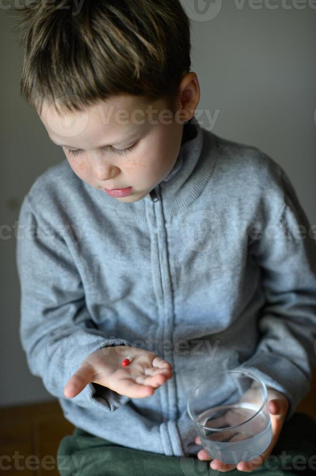 A little boy with a serious expression holds a pill in his hand. photo