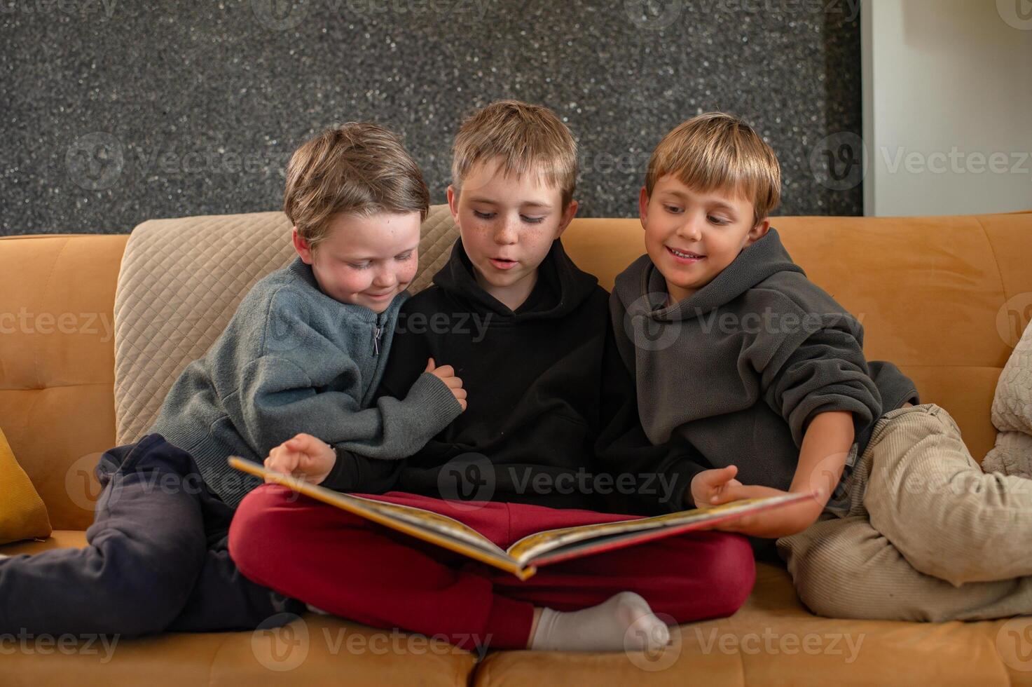 A warm family moment as an older boy reads a bedtime story to his two younger siblings on a cozy couch. photo