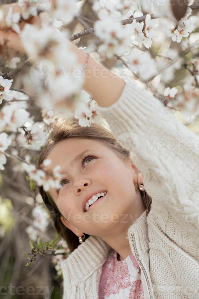 In a serene moment, the girl stands in front of a blooming almond tree, her soft expression captured against the backdrop of vibrant white and pink blossoms photo