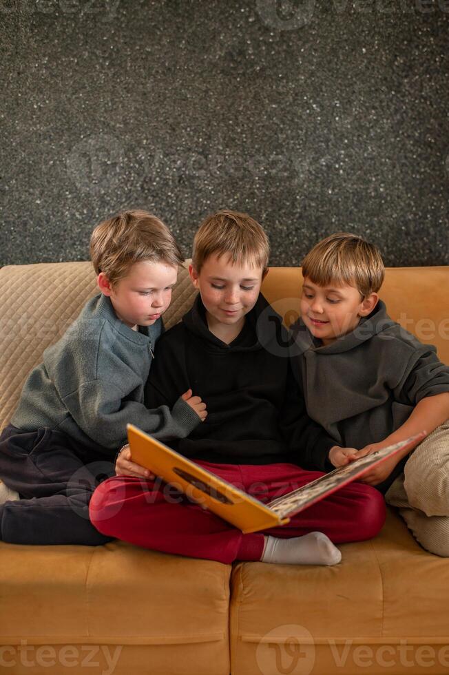An older boy gently turns the pages of a book while his younger brothers sit beside him, eager to hear more. photo