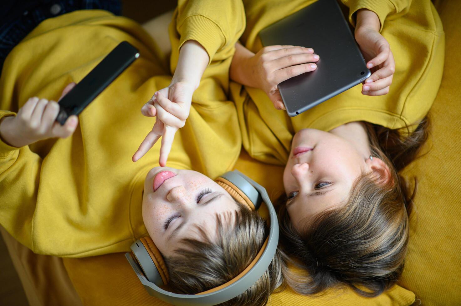 The siblings relax on the sofa, immersed in their screens with headphones on. photo