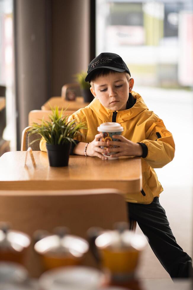 The cafe hums softly around him, but the boy remains still, fingers wrapped around his coffee cup. photo