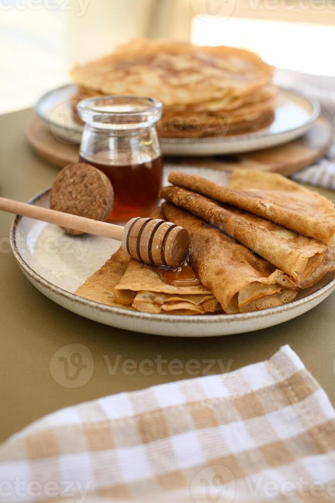 Freshly made pancakes with honey dripping from a honey dipper sit on a countryside table, creating a cozy summer breakfast scene photo