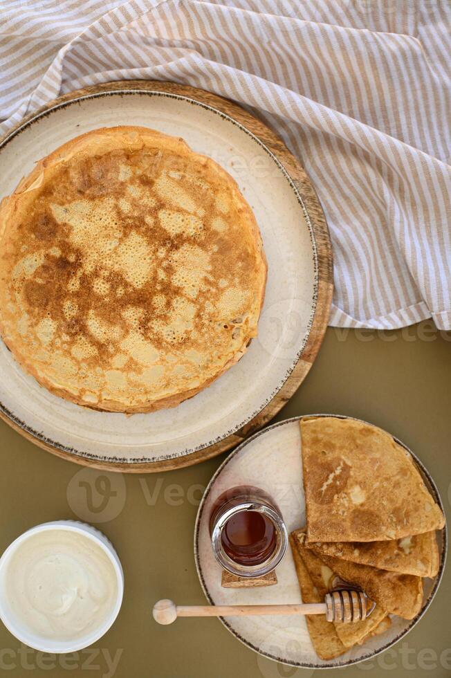 A stack of golden pancakes is drizzled with honey, with a dollop of sour cream on the side, beautifully presented on a rustic plate. photo