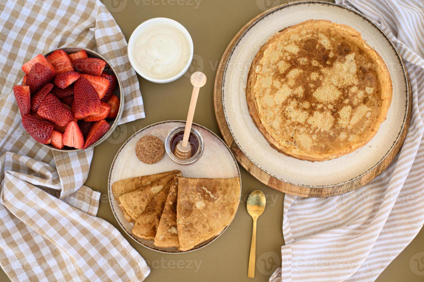 Crispy-edged pancakes with a honey dipper resting on top, paired with a bowl of sour cream and fresh strawberries, creating a perfect balance of flavors photo