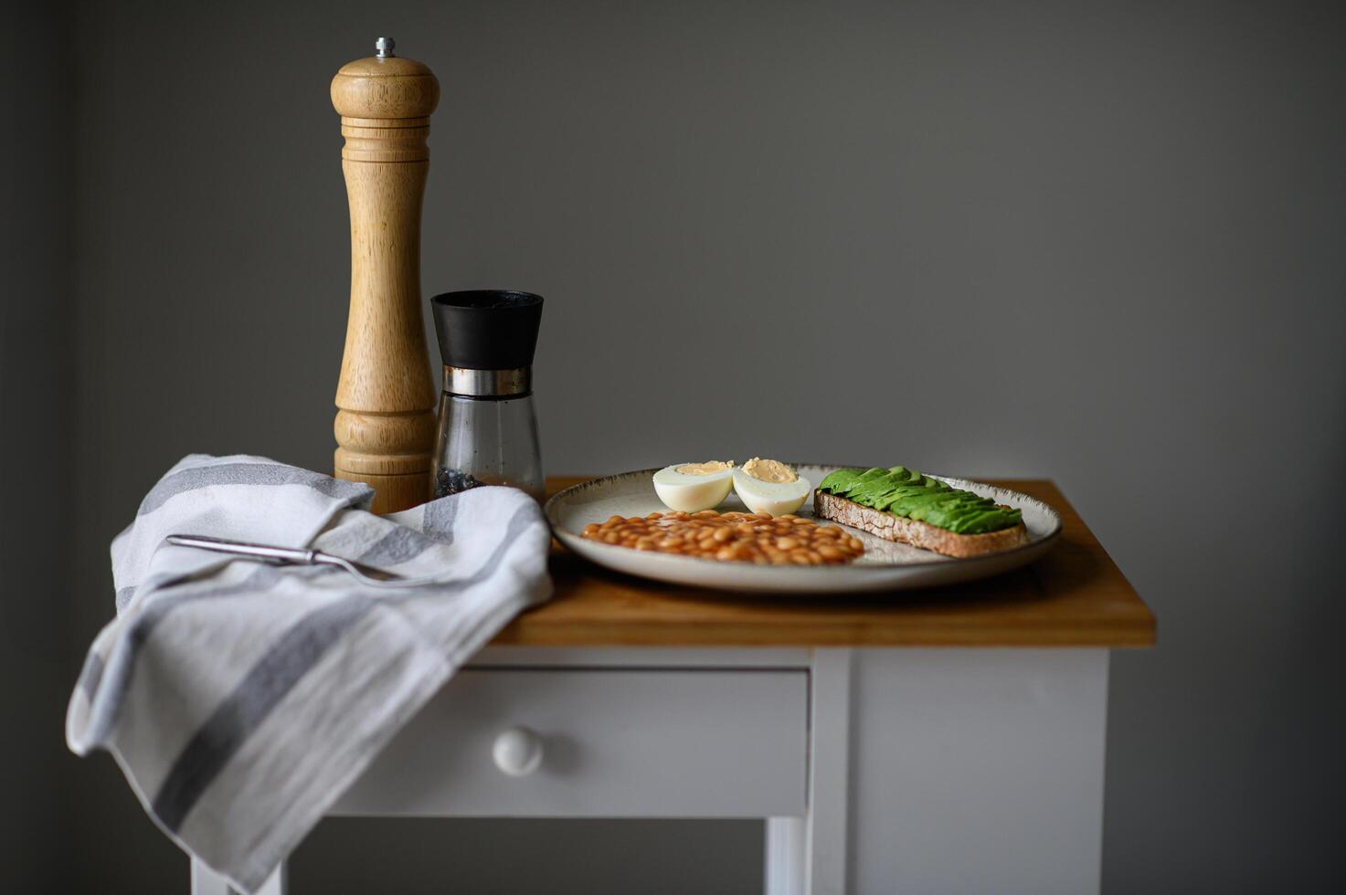 A beautifully arranged morning meal featuring a golden fried egg, creamy avocado toast with black salt, and flavorful white beans in rich red sauce. photo