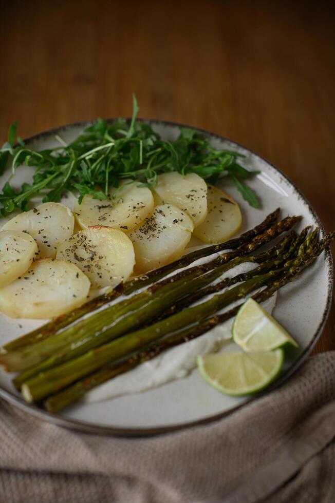 A fresh and flavorful plate of asparagus resting on a buttery sauce, served with crispy potatoes, arugula, and a wedge of lime for extra zest. photo