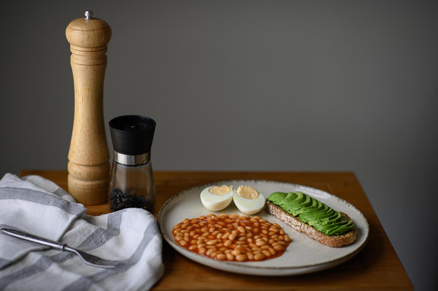 A healthy and satisfying breakfast plate with protein-rich beans, a runny egg yolk, and a flavorful avocado toast. photo