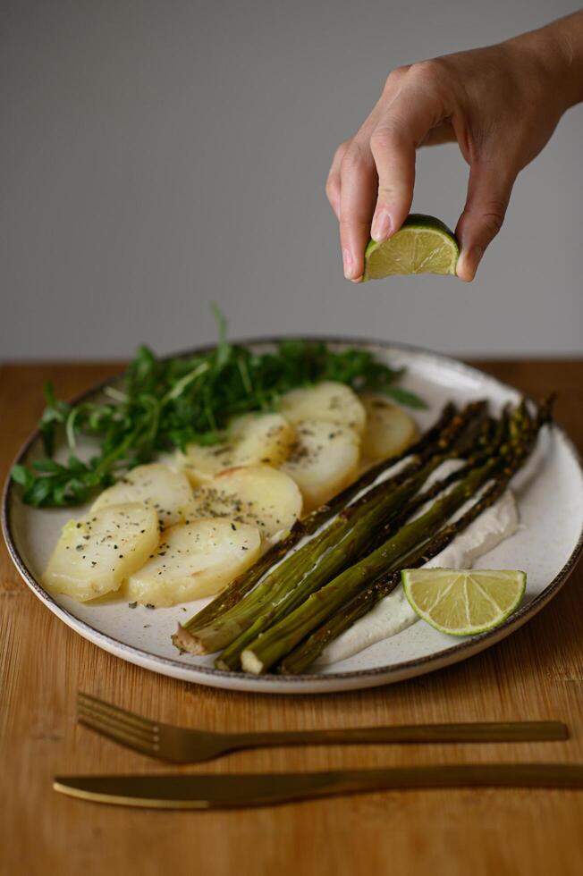 A beautifully plated meal of asparagus, creamy sauce, and crispy potatoes gets a zesty touch from freshly squeezed lime. photo