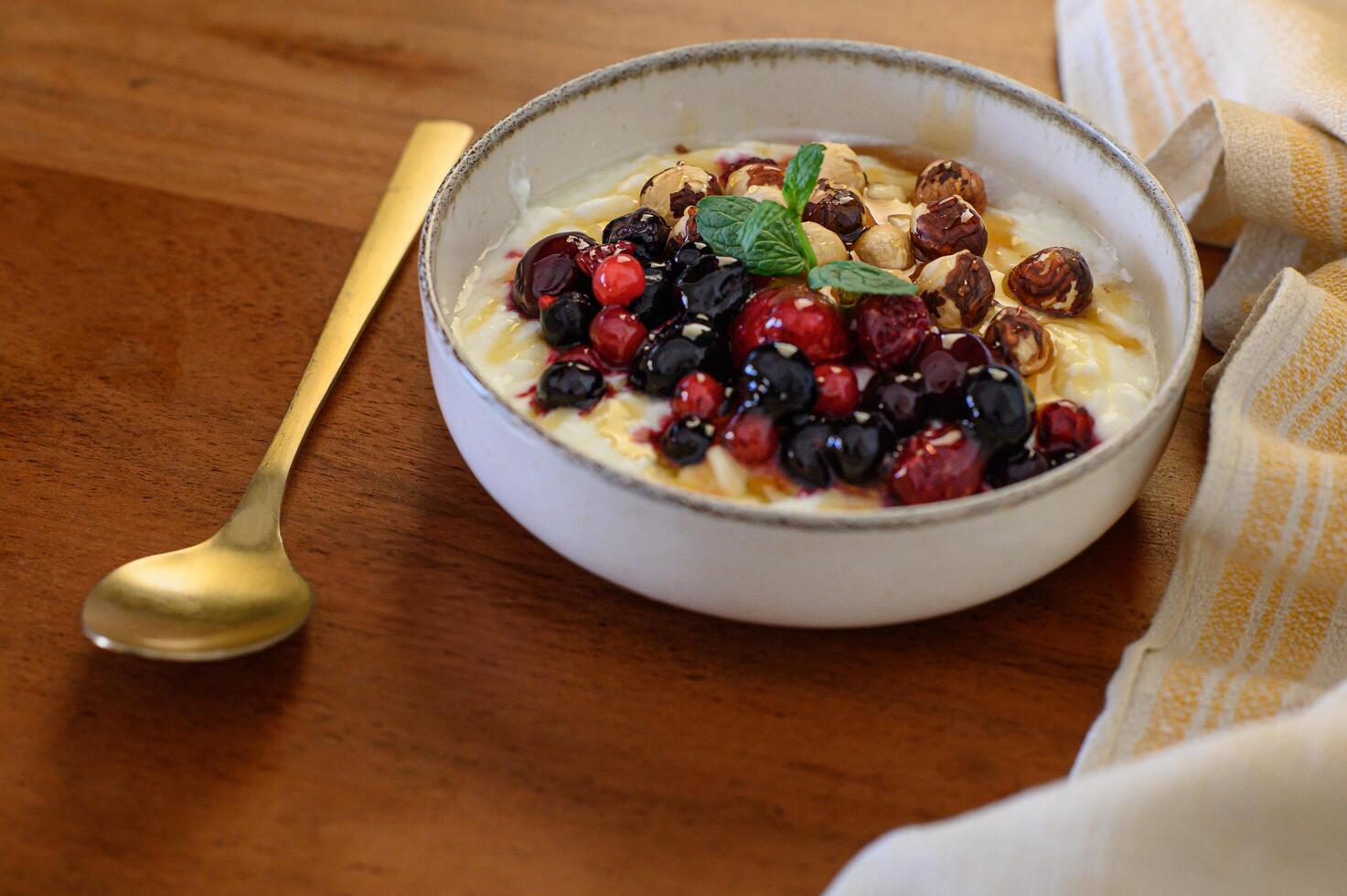 A bowl of yogurt topped with fresh berries, nuts, and drizzled with honey, accompanied by a spoon and a napkin. photo