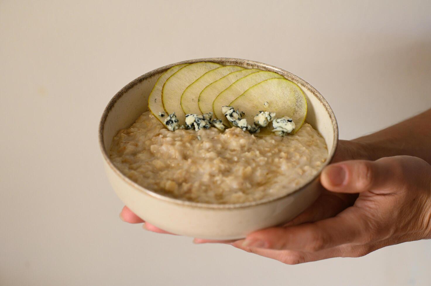 A bowl of creamy oatmeal topped with sliced pear, crumbled Gorgonzola, and a drizzle of honey, styled as a food photo. photo
