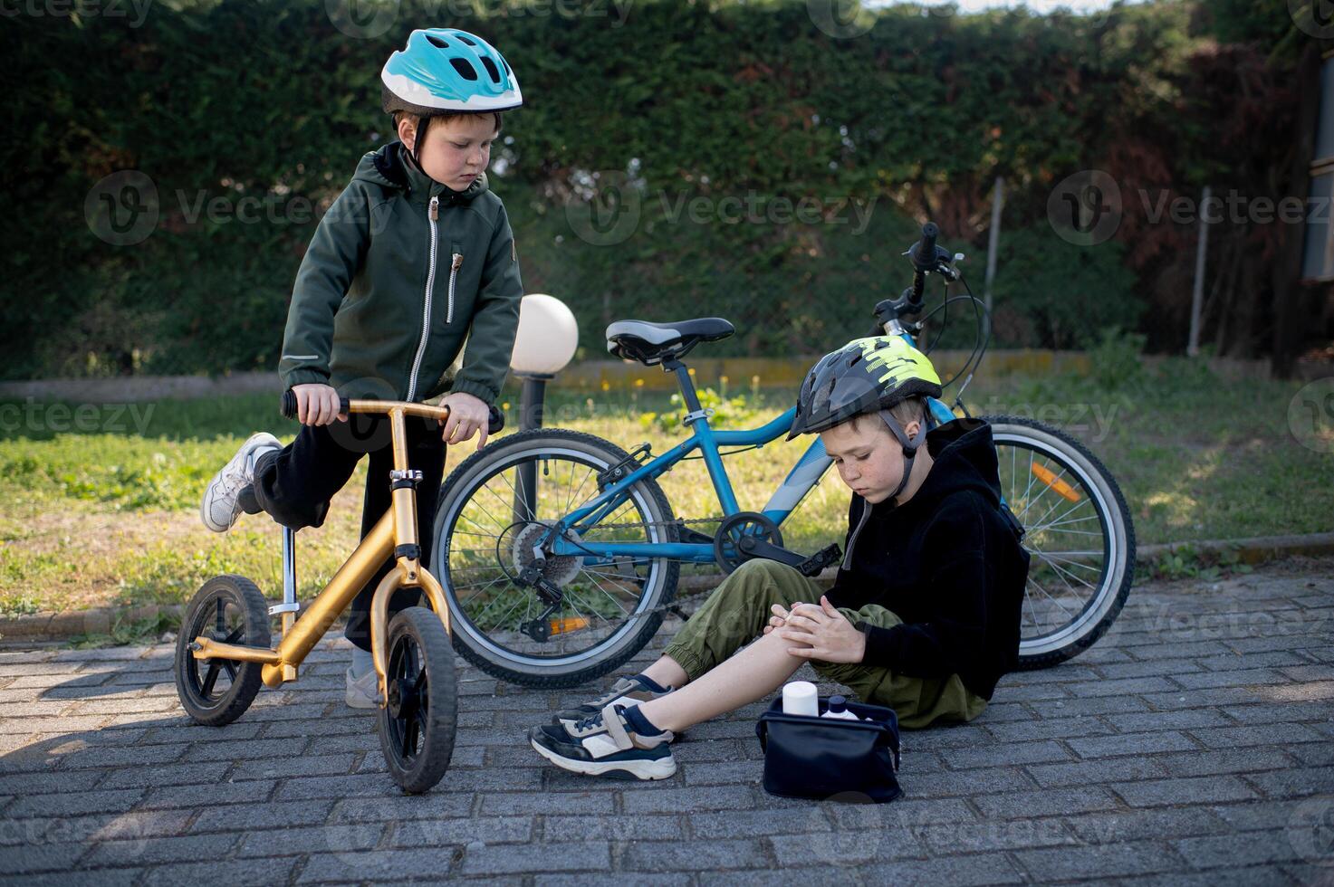 Two small cyclists take a break while one puts a plaster on his scraped knee after a minor fall. photo