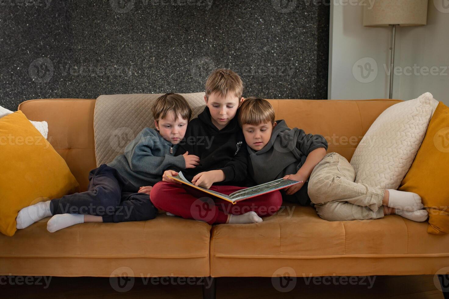 An older boy reads a book to two little boys on the sofa, their faces showing interest and excitement. photo