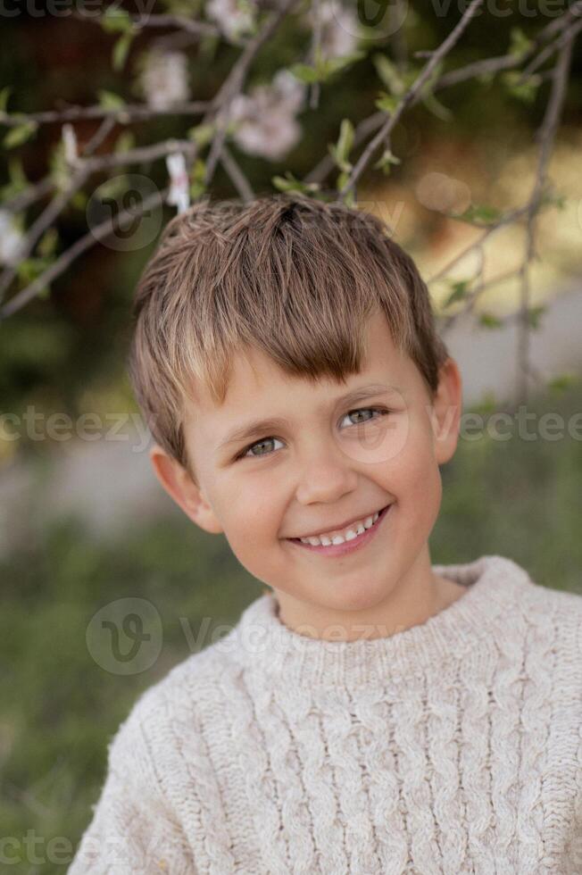 The blonde boy in a white sweater smiles brightly, his sparkling eyes and warm expression radiating pure innocence and joy. photo