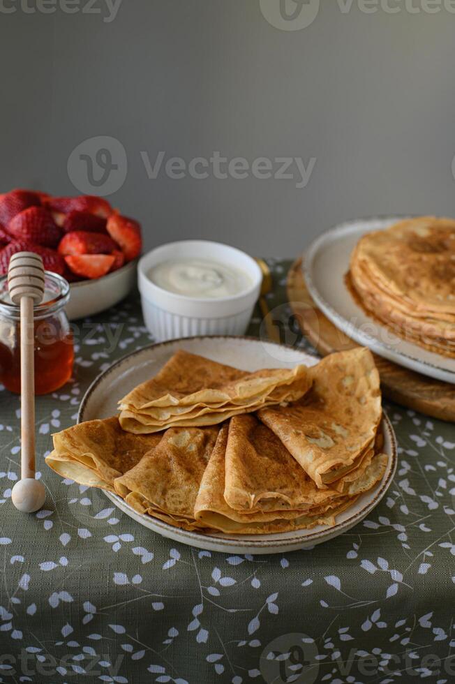 Cozy pancake breakfast with sweet toppings. A warm, inviting table with a stack of pancakes, drizzled honey, fresh strawberries, and a bowl of sour cream. photo