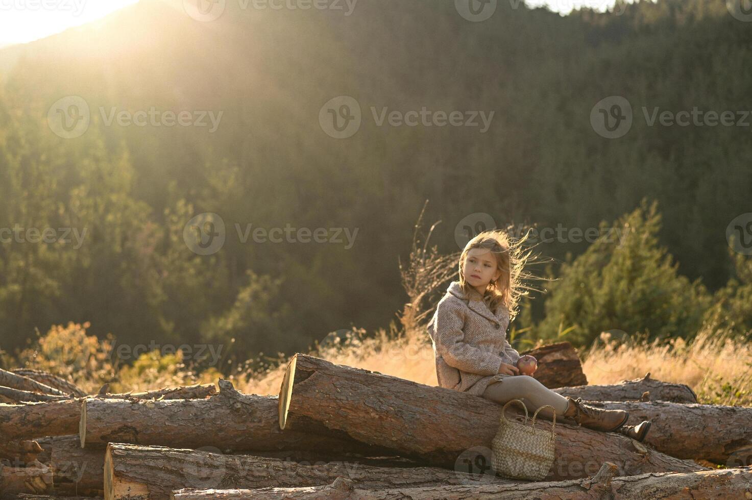 Soft light touches a girl seated on stacked logs in the hills, eating an apple and enjoying the stillness photo