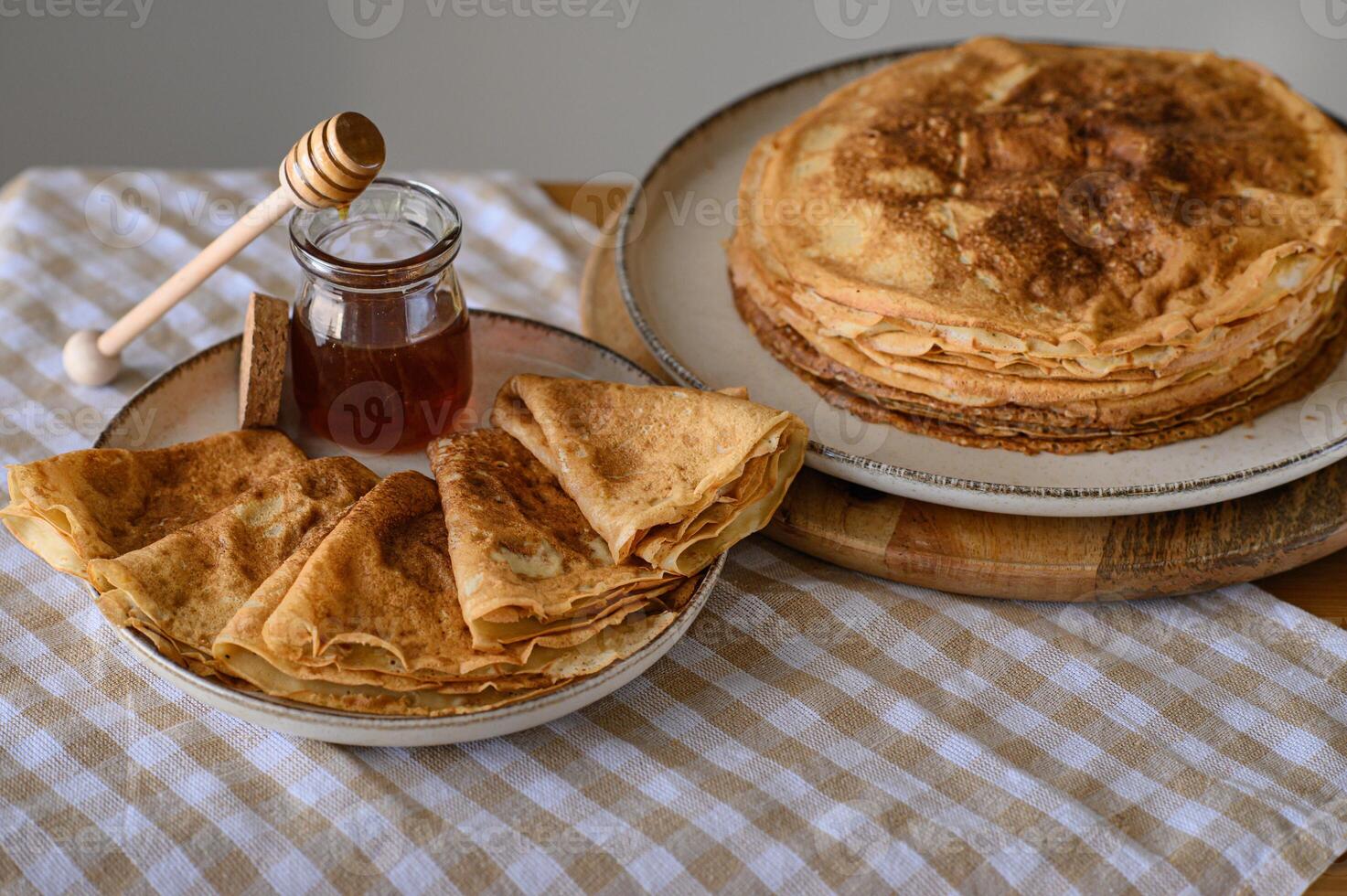 Golden pancakes with honey on a light tablecloth. A stack of warm, golden-brown pancakes served with a jar of honey and a wooden honey dipper on a soft, light tablecloth. photo