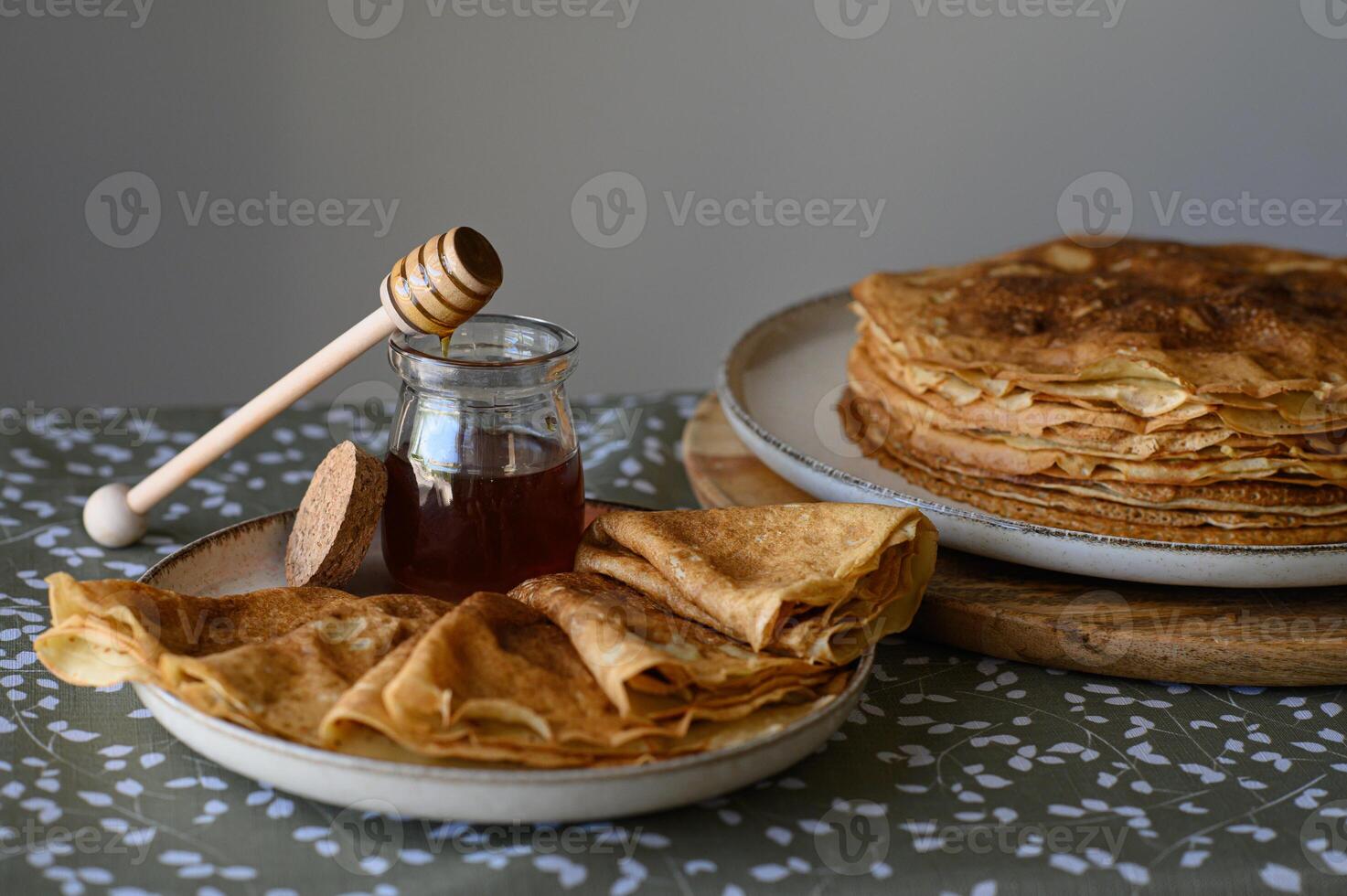 Delicate crepe with honey drizzle on a cozy table. A thin, homemade crepe is gently folded, with honey dripping from a wooden dipper onto its golden surface. photo