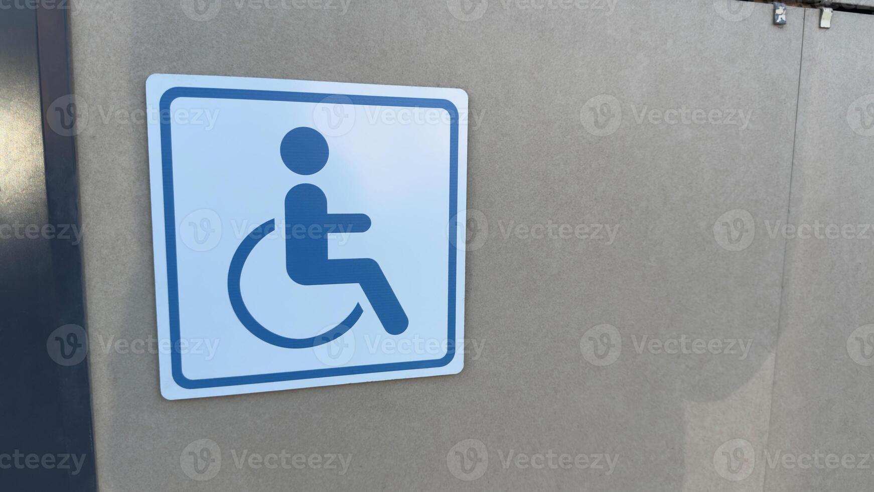 Blue sign of disabled person in wheelchair on wall of building. Concept of creating accessible areas. Mobility defects of person in wheelchair and protection rights of people with disabilities photo