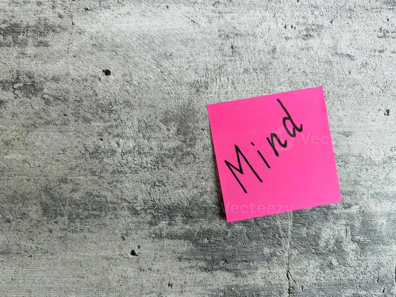 Vibrant pink sticky note with the word Mind placed on a textured grey background, representing mental clarity, focus, and the significance of mindfulness in personal and professional life photo