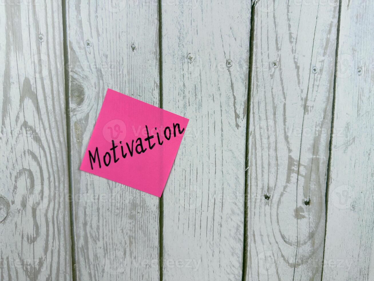 Pink sticky note with the word Motivation written on it, pinned on a white wooden board background. The image symbolizes inspiration, drive, and determination. Excellent for concept themes photo