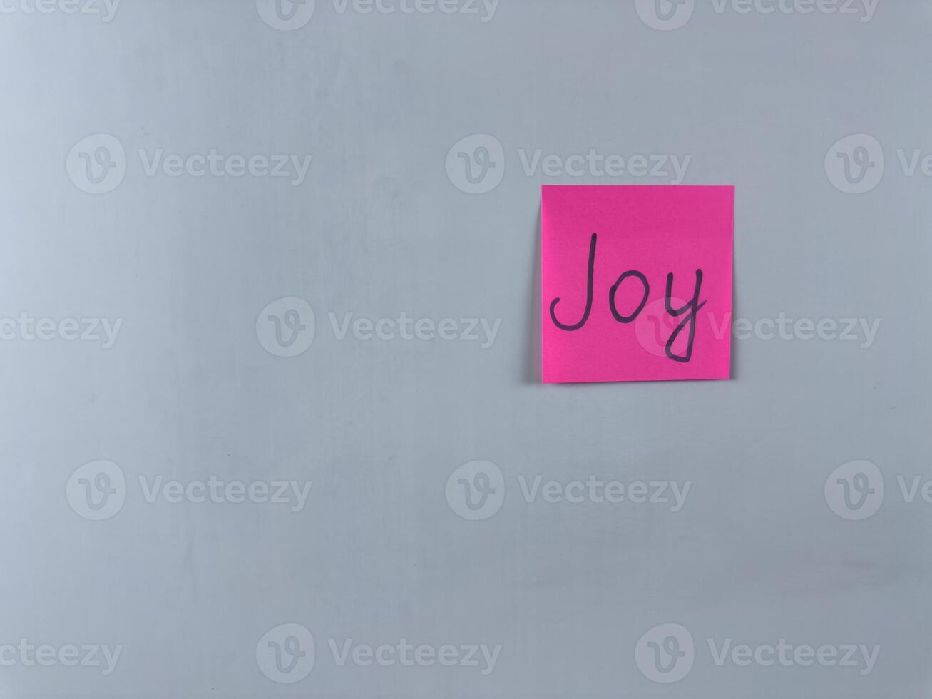 Sticky note with Joy written on it, affixed to a white background. Photo represents happiness and delight, ideal for themes of joy and positive emotions