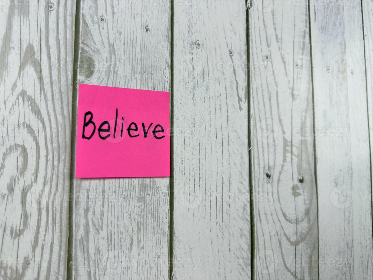 Pink sticky note with Believe written on it, placed on white wooden board. Ideal for conveying themes of belief, positivity and motivation. Perfect for concept ideas and personal growth photo
