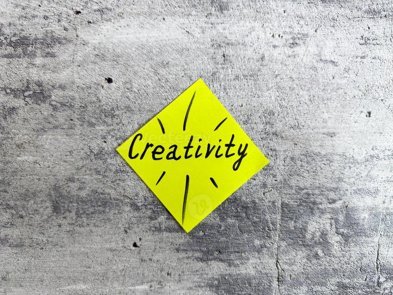 Vibrant yellow sticky note shaped as a diamond displaying the word Creativity and decorative elements on a textured grey background, representing the essence of innovative thinking and inspiration photo
