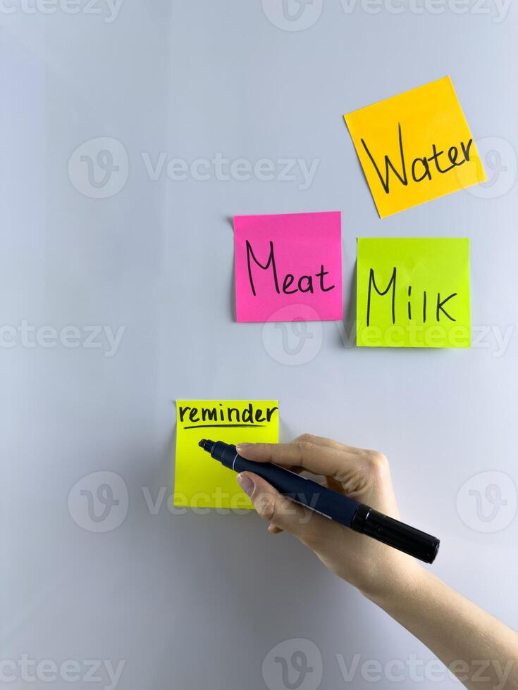 Girl writes reminder with marker on colored sticky note on refrigerator photo