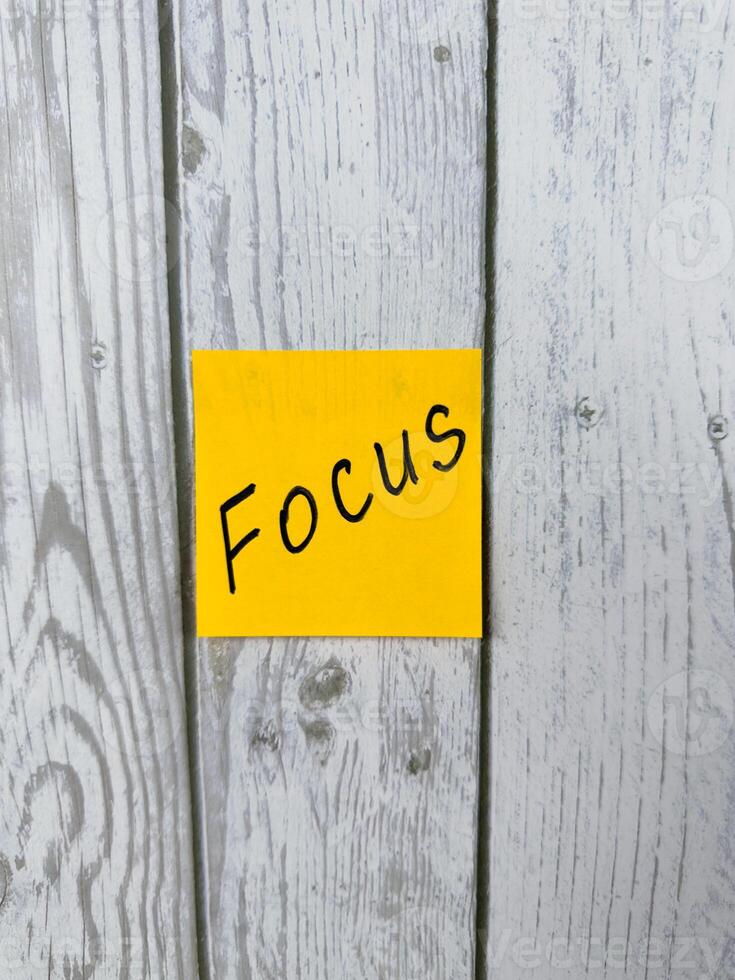 Sticky note with Focus written on it, placed on white wooden board. Ideal for conveying themes of concentration, proactive mindset, productivity, and goal achievement photo