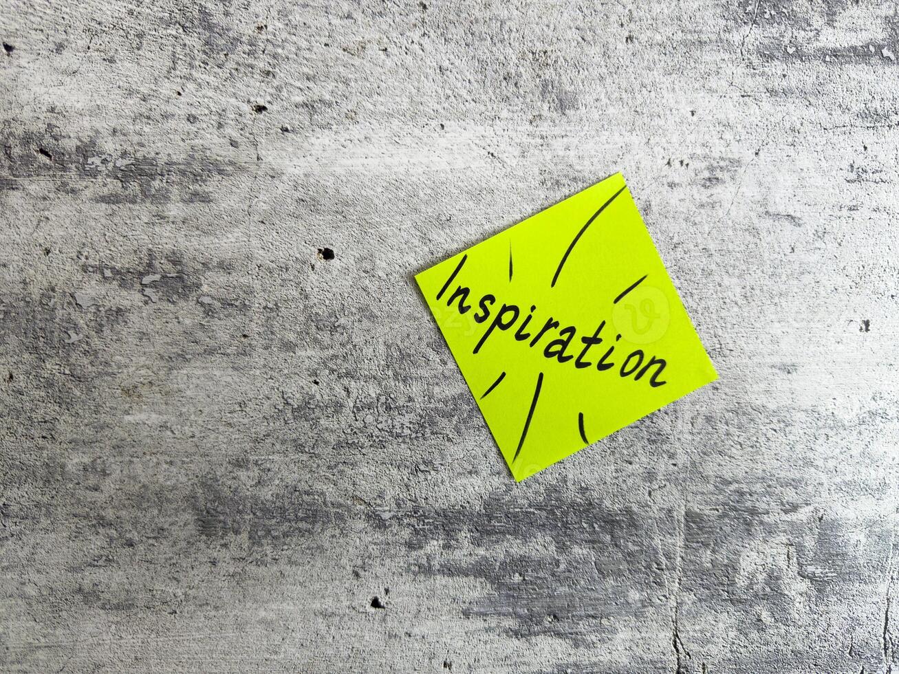 Bright yellow sticky note shaped as a diamond featuring the word Inspiration and decorative elements on a textured grey background, symbolizing the power of motivating ideas and creativity photo