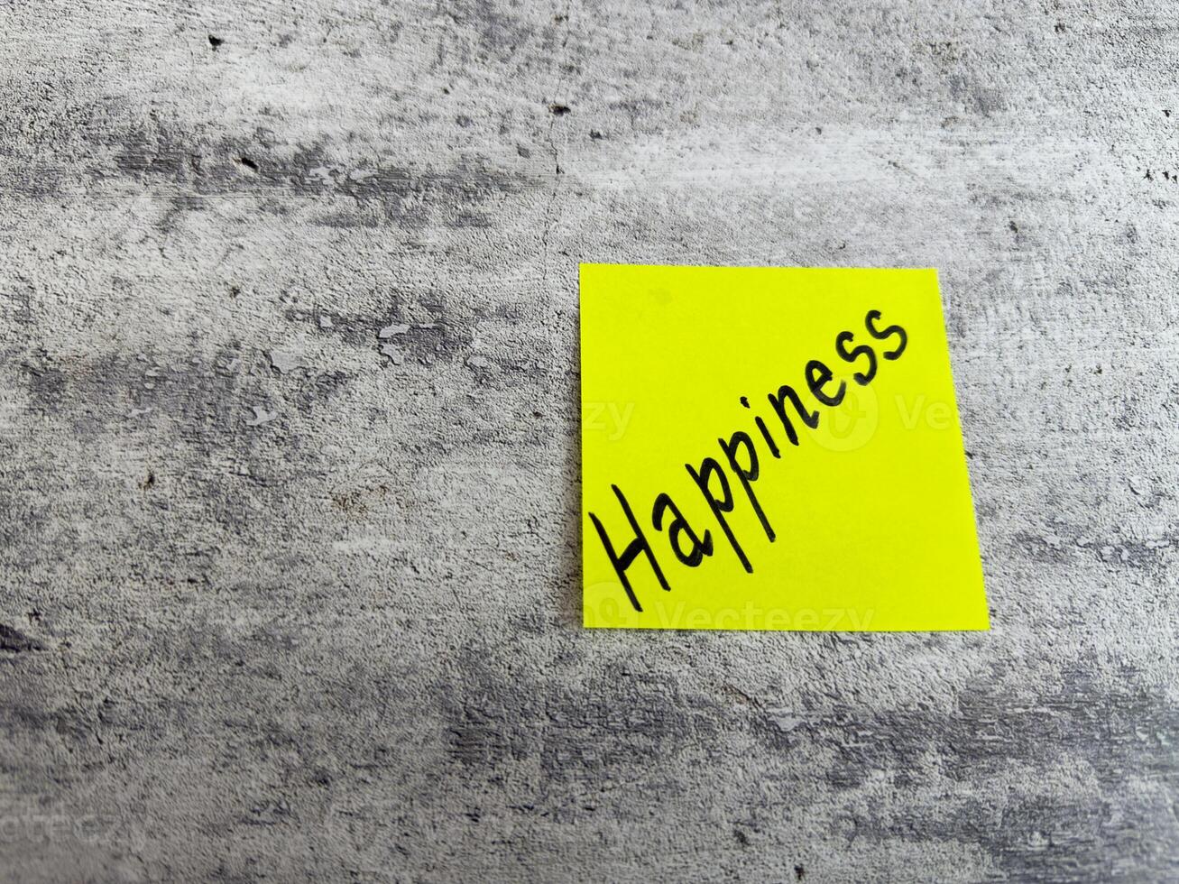 Vivid yellow sticky note displaying the word Happiness against a textured grey background, symbolizing the importance of joy and positivity in everyday experiences and personal growth photo