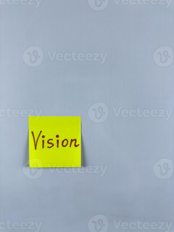 Sticky note with Vision written on it, affixed to white background. Photo represents foresight and goals, ideal for themes of vision and future aspirations
