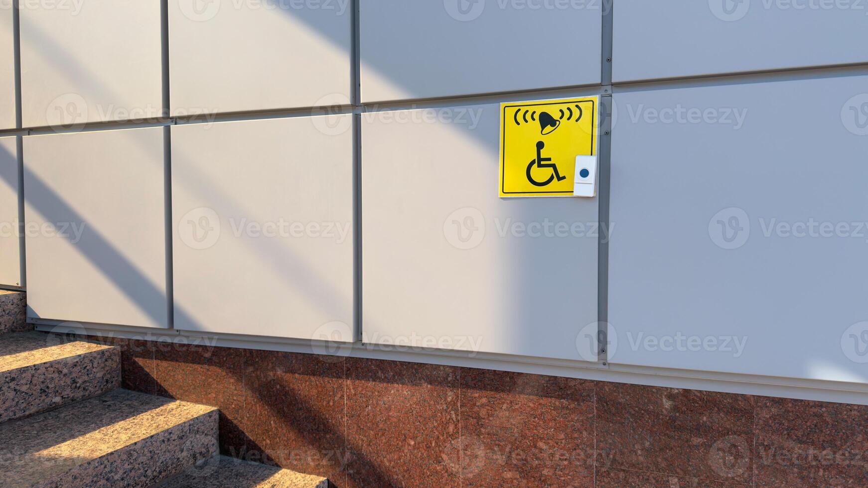 Plate with image of disabled person in wheelchair and call button. Disabled person sign and button for help in front of entrance to building near stairs, social concept of help disabled person photo