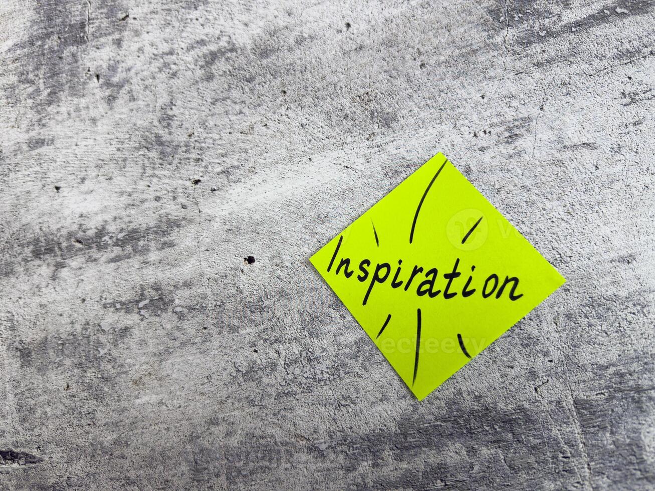 Vibrant yellow sticky note in a diamond shape displaying the word Inspiration with decorative elements on textured grey surface, representing the essence of motivating ideas and creative potential photo