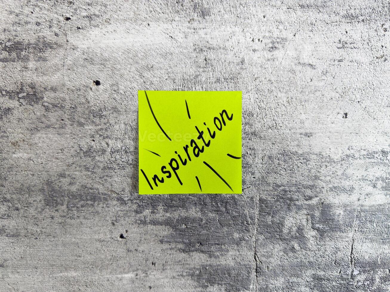 Vibrant yellow sticky note shaped as a rectangle displaying the word Inspiration with decorative rays on a textured grey background, acting as a symbol of creativity and motivating ideas photo