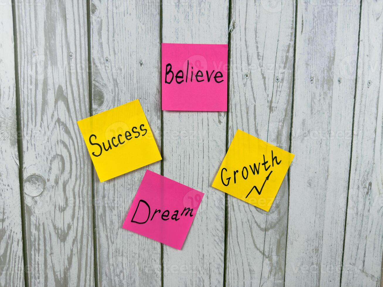 Colorful sticky notes with inspirational words pinned on white wooden board background. Perfect for illustrating concepts of motivation, achievement, and personal growth photo