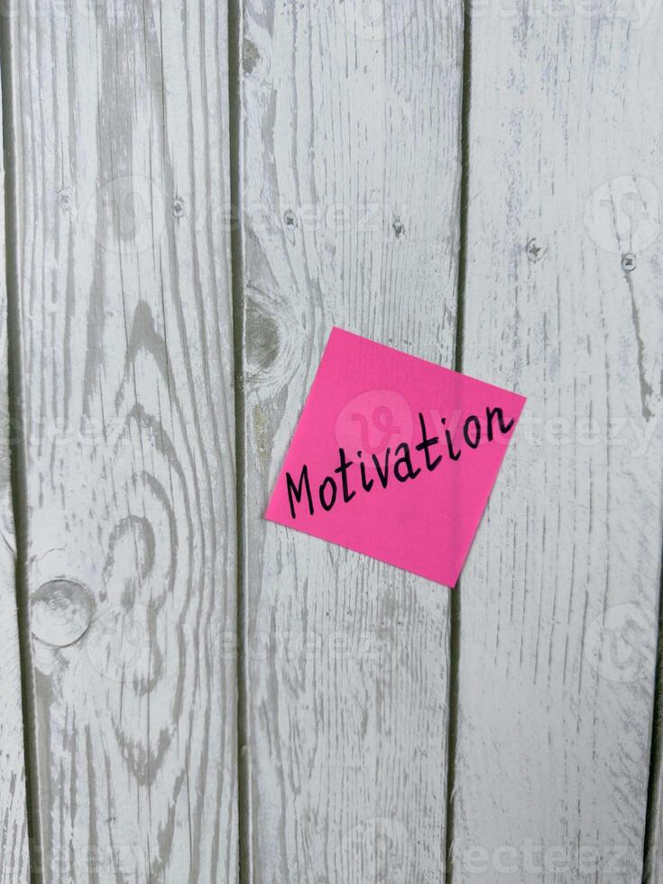 Pink sticky note with the word Motivation written on it, placed on a white wooden background. Ideal for themes of inspiration, determination, and achieving goals. Perfect for motivation concept photo