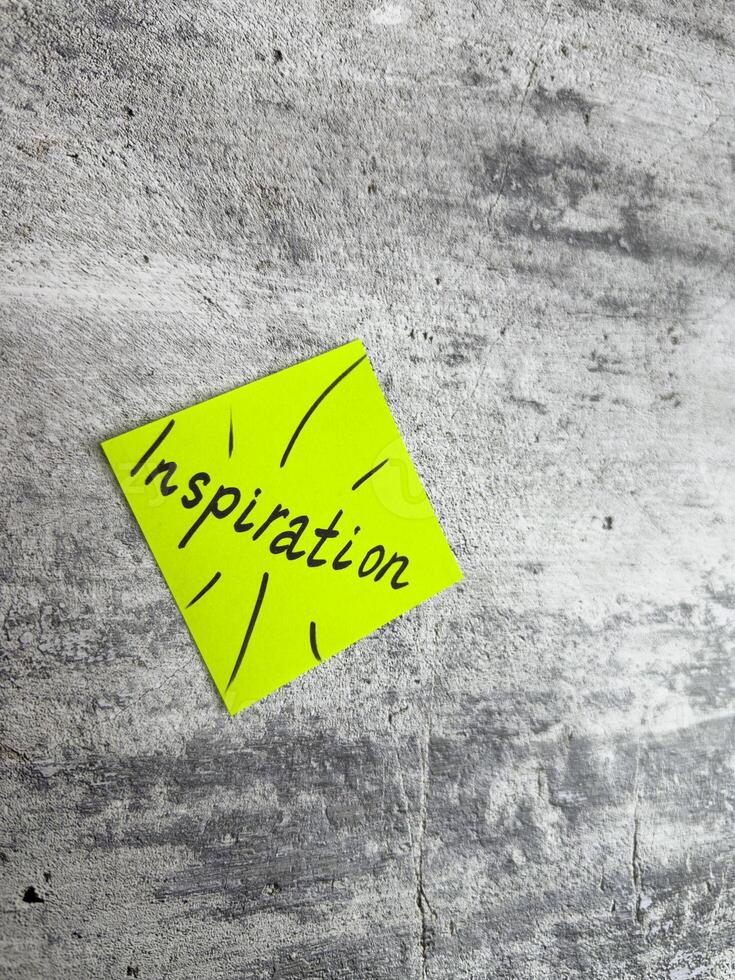 Bright yellow sticky note in a diamond shape featuring the word Inspiration and decorative rays on a textured grey background, symbolizing the spark of creativity and motivating ideas photo