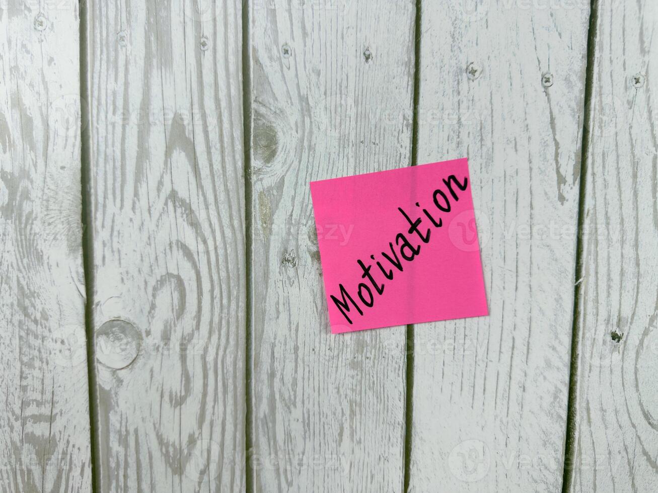 Pink sticky note with Motivation written on it, placed on a white wooden board. This image symbolizes motivation and commitment, ideal for conveying themes of drive and determination photo
