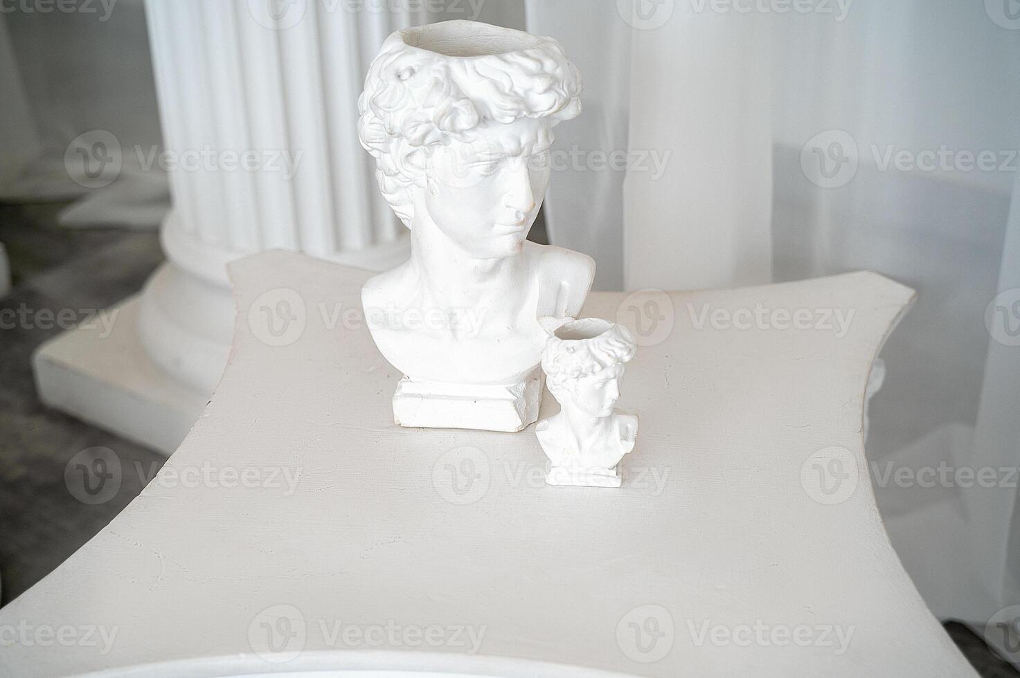 photo zone for photo sessions in antique and greek style antique sculptures in the interior. two plaster sculptures stand on the table. behind white chiffon fabric and columns