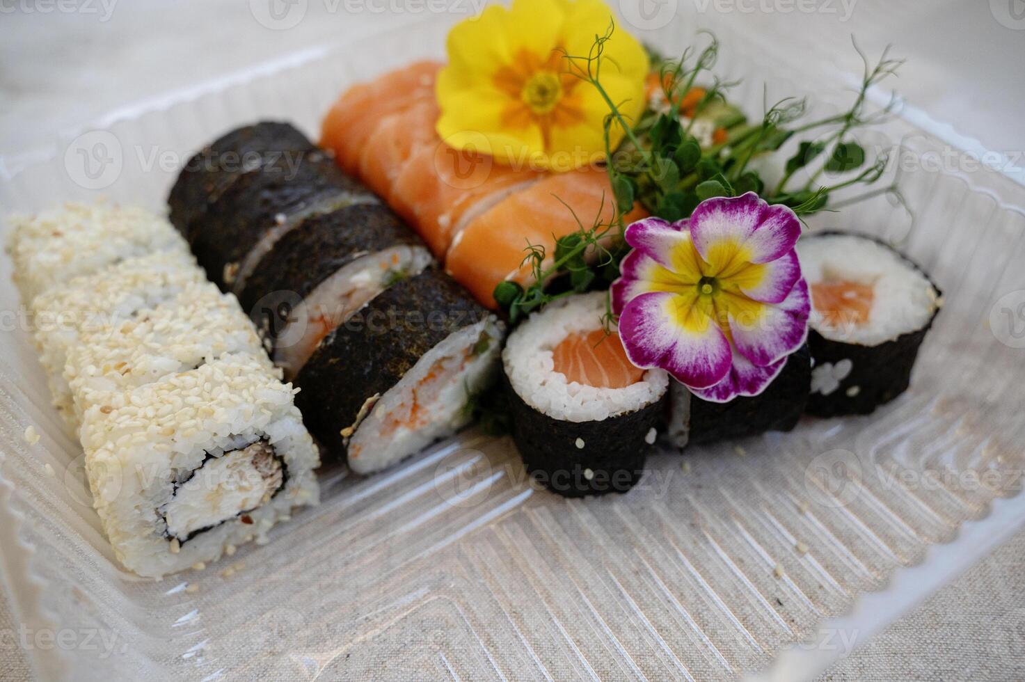 Mix of sushi rolls with salmon, avocado, smoked eel, in a plastic food delivery box. food delivery concept. sushi bar menu. transparent plastic lunch box with sushi set. sushi decorated with flowers. takeaway food photo