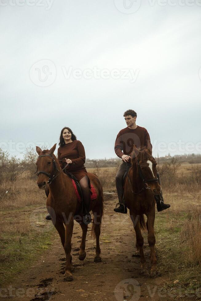 Young romantic couple horse riding, against the background of a field with autumn grass. They gallop across the fields, stylishly dressed in brown shades. They smile and are happy during a romantic honeymoon. photo