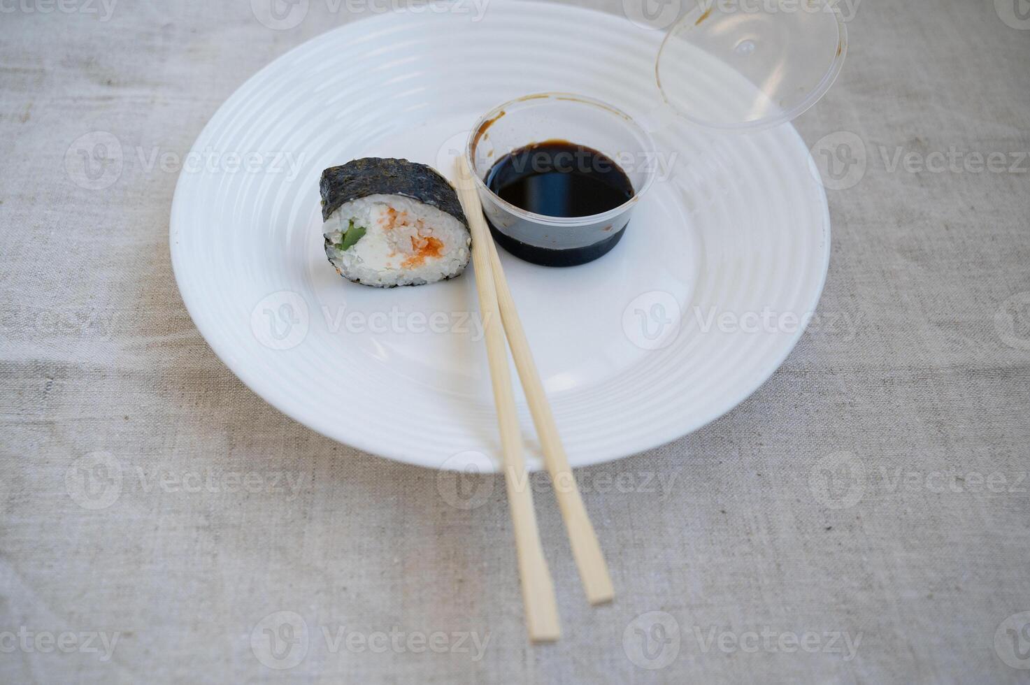 sushi roll with chopsticks and wasabi sauce in a plastic container on a white plate. elements of japanese cuisine, takeaway food. linen tablecloth on the table. high quality photo